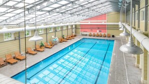 Une grande piscine intérieure dotée de plusieurs couloirs de nage, de chaises longues et d’un système d’éclairage au plafond.