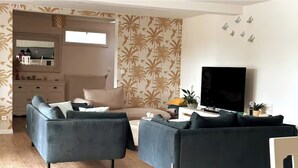 A modern living room with two sofas, a coffee table, and a TV. There is a kitchen visible through an open doorway. - Quiet House (Amiens)