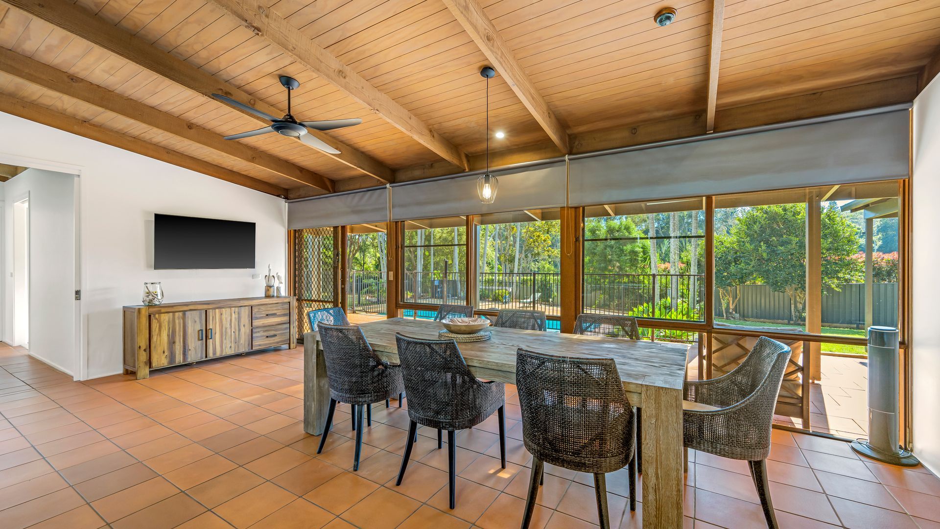 A spacious kitchen with a large dining table, wicker chairs, and a TV mounted on the wall.