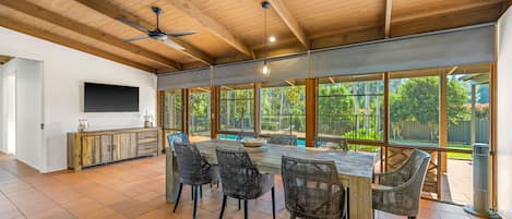 A spacious kitchen with a large dining table, wicker chairs, and a TV mounted on the wall.