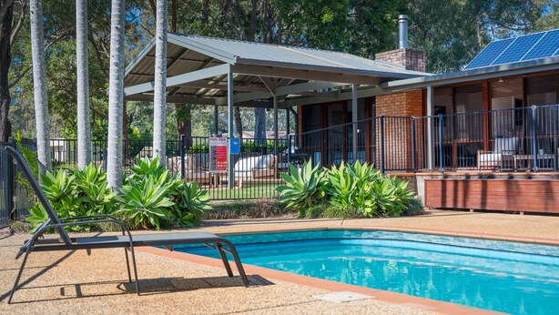 A swimming pool with a covered seating area, surrounded by greenery and a fence. - Koalas at Links Lighthouse Beach (Port Macquarie)
