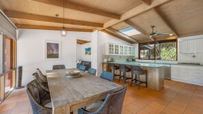 A spacious kitchen with white cabinets, a central island with bar stools, and a dining area with a wooden table and wicker chairs.