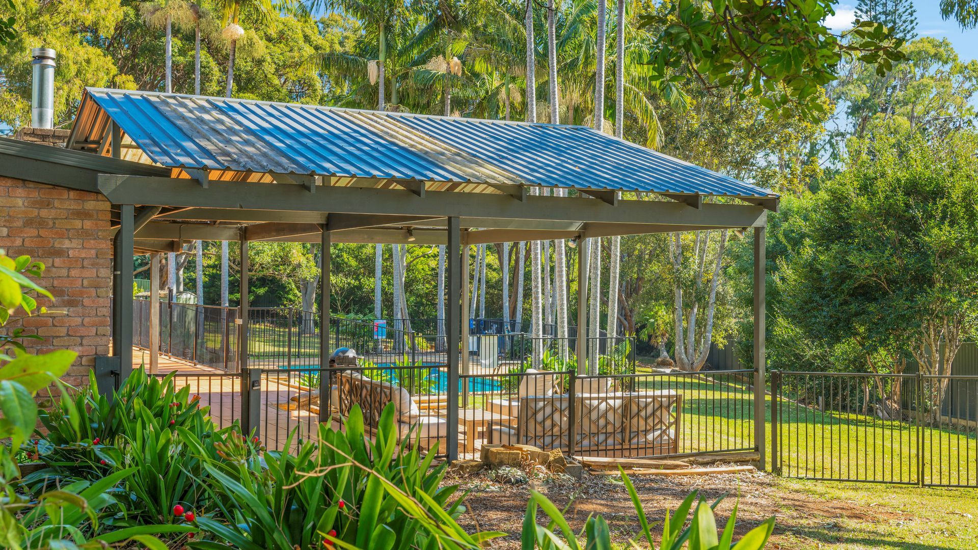 A covered outdoor area with a pool, surrounded by a fence and trees.