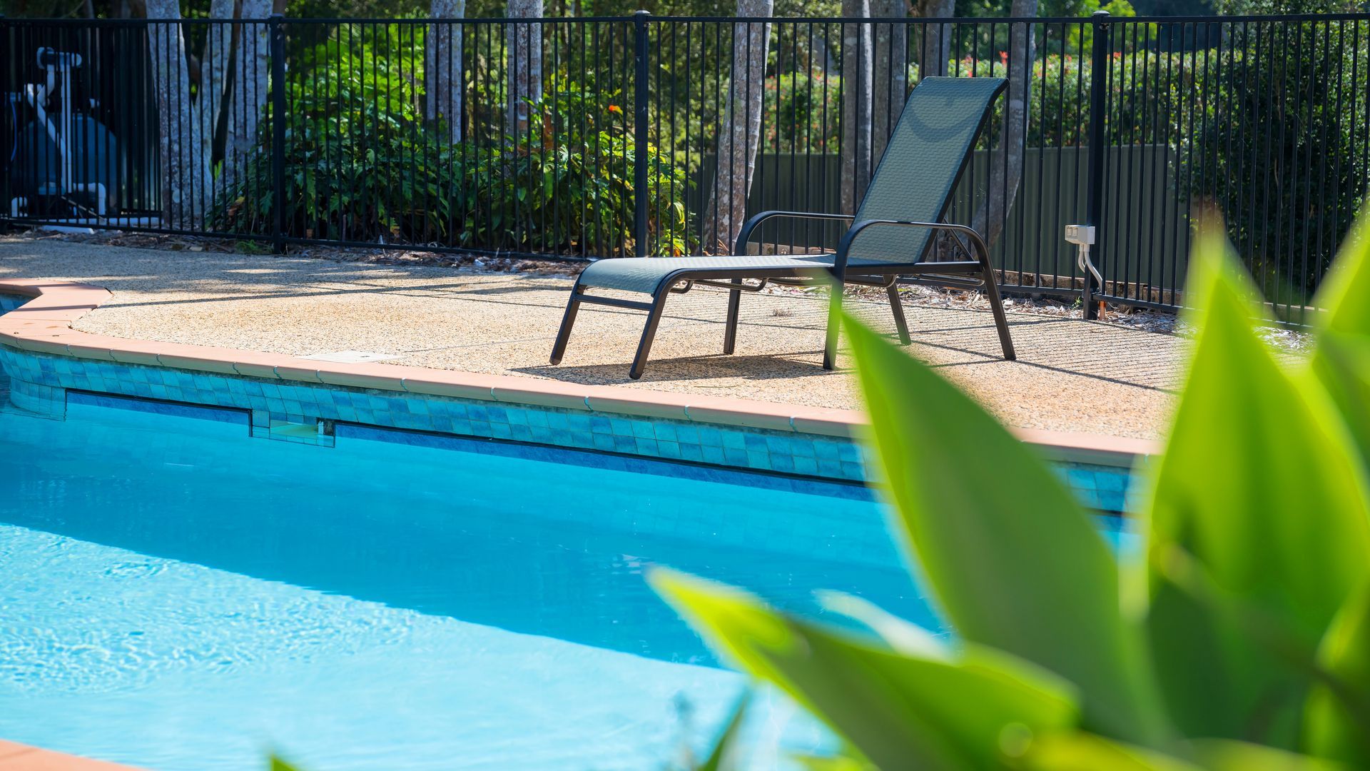 A swimming pool with two lounge chairs and a fence in the background.