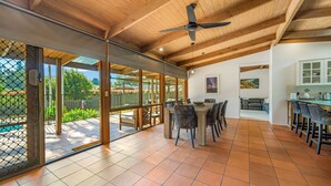 A spacious dining area with a large table and chairs, a ceiling fan, and a view of the outdoors through large sliding glass doors. - Koalas at Links Lighthouse Beach (Port Macquarie)