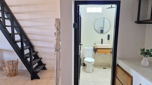Ein modernes Badezimmer mit Toilette, Waschbecken und Spiegel. Eine Holztreppe führt in einen anderen Raum.