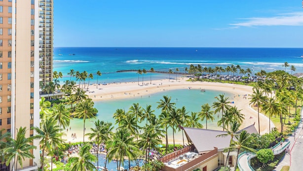 A beachfront hotel with a pool, beach, and palm trees.