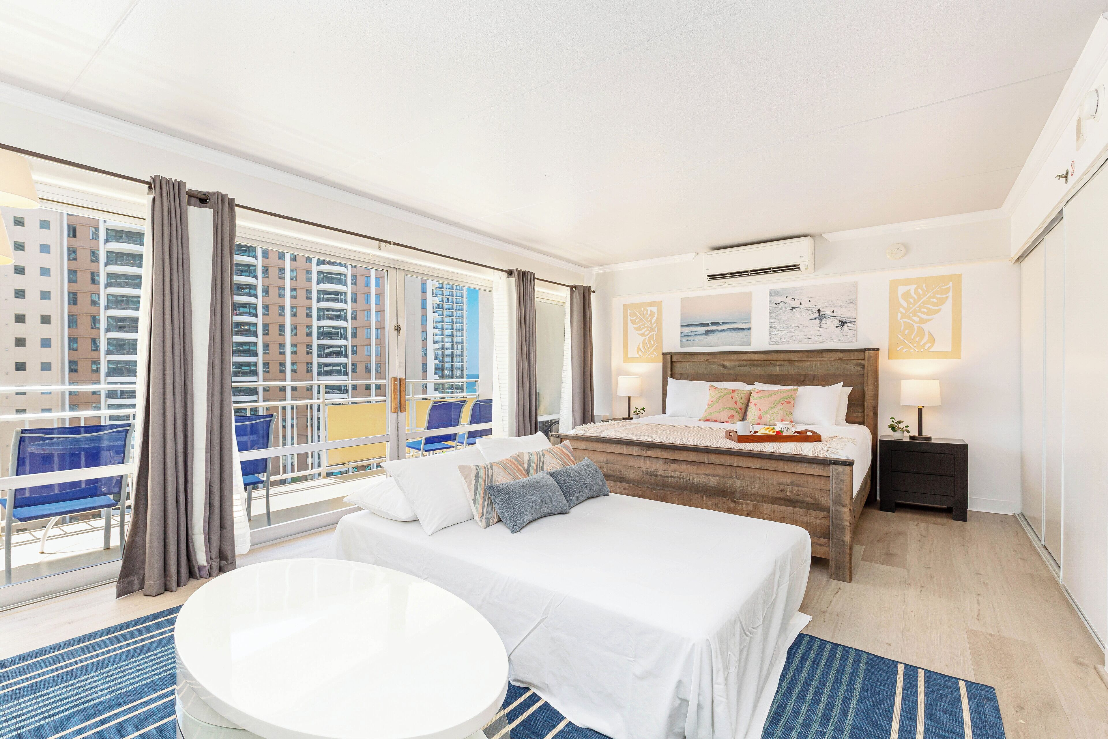 Ein Hotelzimmer mit einem großen Bett, einem runden Tisch und Blick auf eine Stadtlandschaft durch raumhohe Fenster.