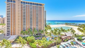 A high-rise hotel with multiple balconies overlooking a beach and a pool area.