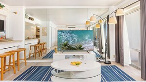 A modern kitchen with a large island, wooden stools, and a large TV screen.