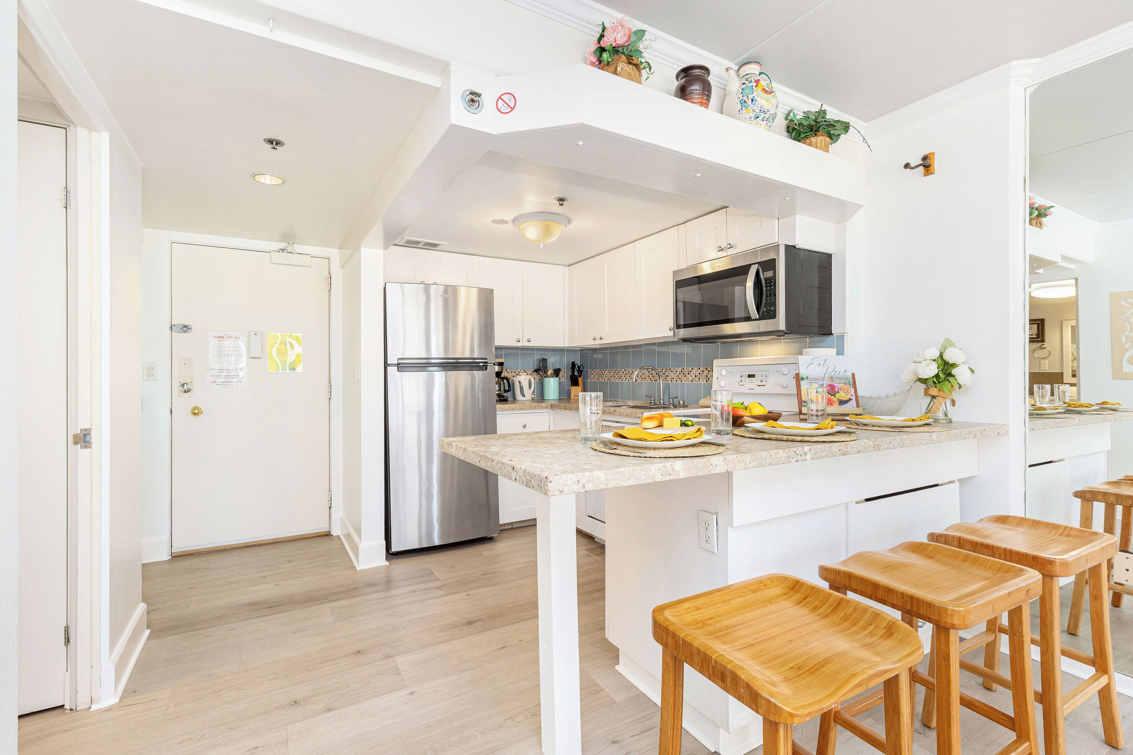 A modern kitchen with white cabinetry, stainless steel appliances, and wooden stools.