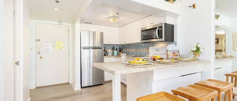 A modern kitchen with white cabinetry, stainless steel appliances, and wooden stools.
