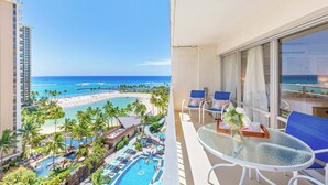 A balcony with a pool, lounge chairs, and a view of a beach and ocean.