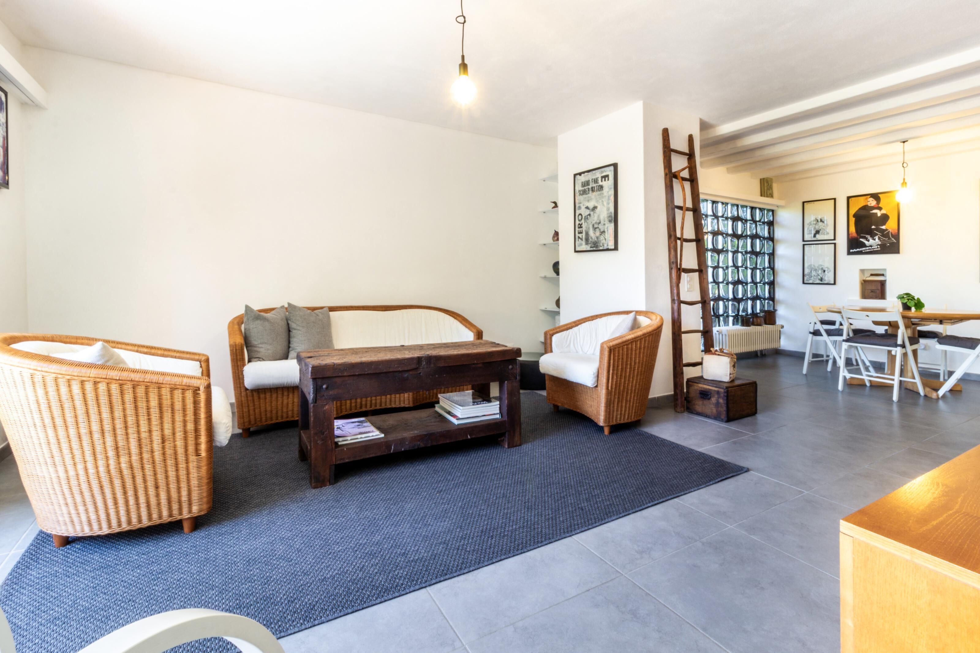 Een woonkamer met rieten meubels, een bijzettafeltje en een ladder tegen de muur.