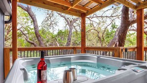 A hot tub with a bottle of wine and two glasses, surrounded by wooden deck and trees. - Good Day Treehouse I Hot tub, stargazing (Wimberley)