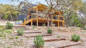 A wooden cabin with a balcony, surrounded by trees and a dry landscape. - Good Day Treehouse I Hot tub, stargazing (Wimberley)