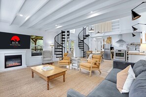 A spacious living room with a fireplace, a spiral staircase, and a kitchen area. - Good Day Treehouse I Hot tub, stargazing (Wimberley)