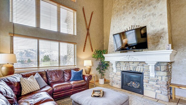 A living room with a stone fireplace, leather sofa, and a flat-screen TV mounted above it. - Hot Tub & Mtn-view Deck: Townhome in Eden (Eden)