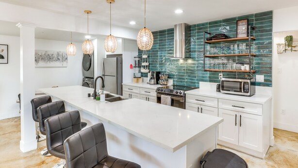 A modern kitchen with a central island, white cabinetry, and a backsplash with green tiles.