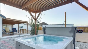 A hot tub under a wooden pergola with a patio area, including chairs and a table.