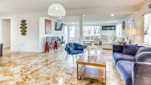 A spacious living room with a marble floor, a blue armchair, a dark sofa, and a wooden coffee table.