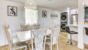 A modern kitchen with a dining area, featuring a white table, floral chairs, a hanging light fixture, and a built-in washing machine.