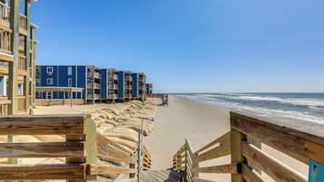 Une promenade en bois mène à une plage, avec un bâtiment bleu en arrière-plan.