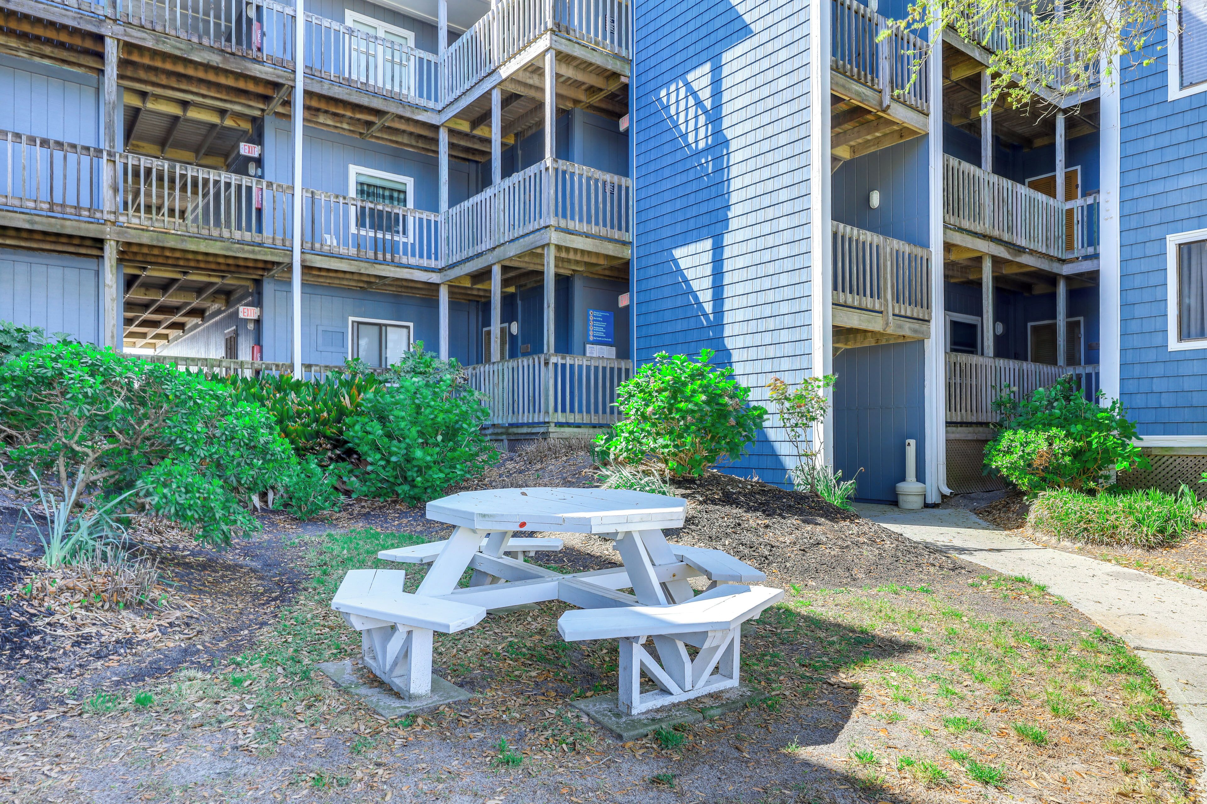 A multi-story building with balconies, a picnic table, and surrounding greenery.