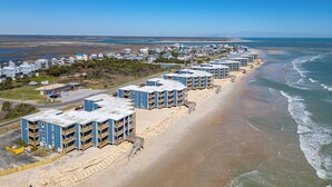A beachfront hotel with multiple-story buildings, a sandy beach, and a clear view of the ocean. - Oceanfront Gem w/ Views in North Topsail Beach (Sneads Ferry)
