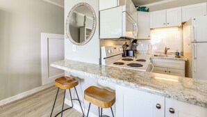 A kitchen with white cabinets, a granite countertop, a stove, and two wooden bar stools. - Oceanfront Gem w/ Views in North Topsail Beach (Sneads Ferry)
