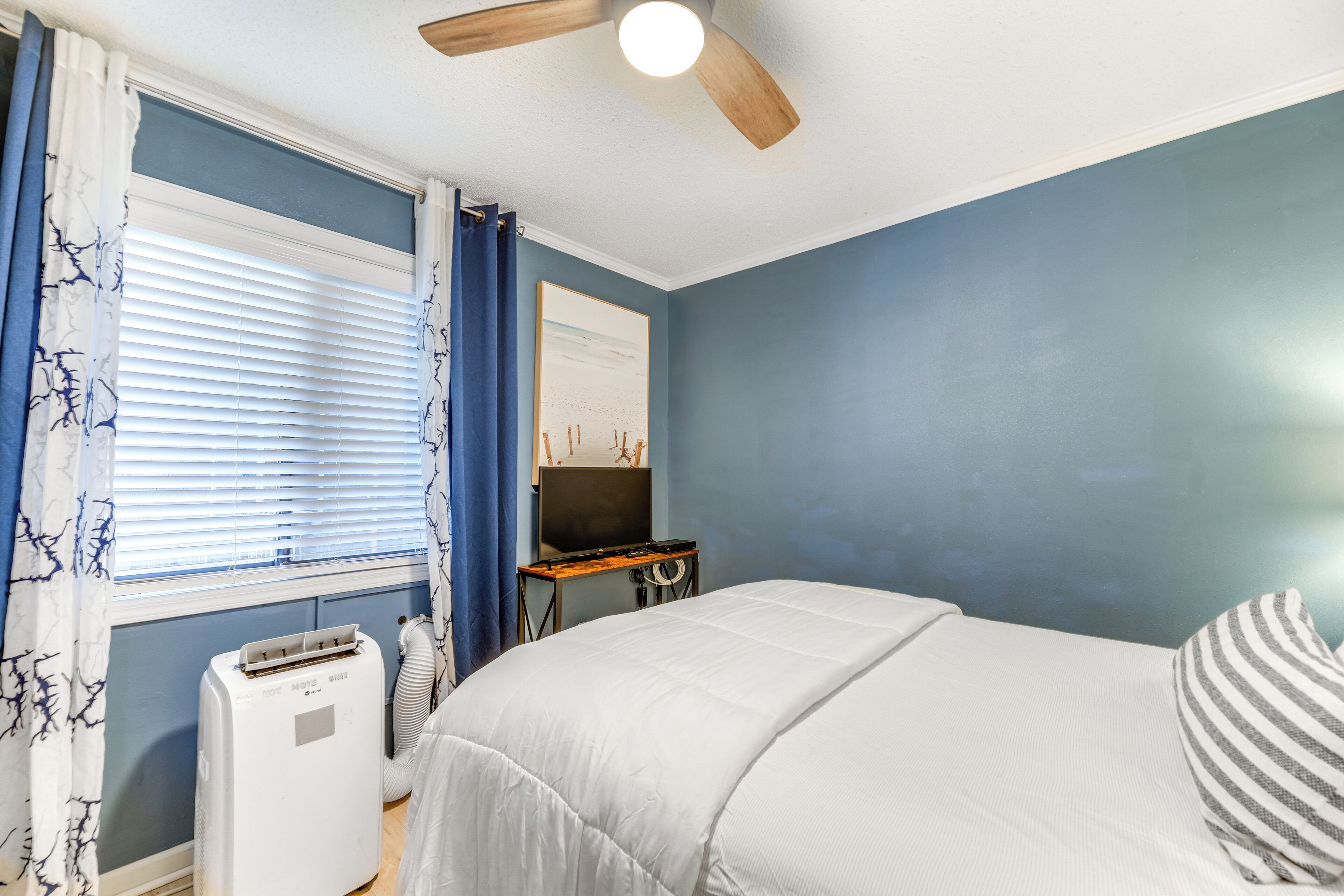 Une chambre à coucher avec un lit, un ventilateur de plafond, un radiateur et un téléviseur posé sur un meuble.