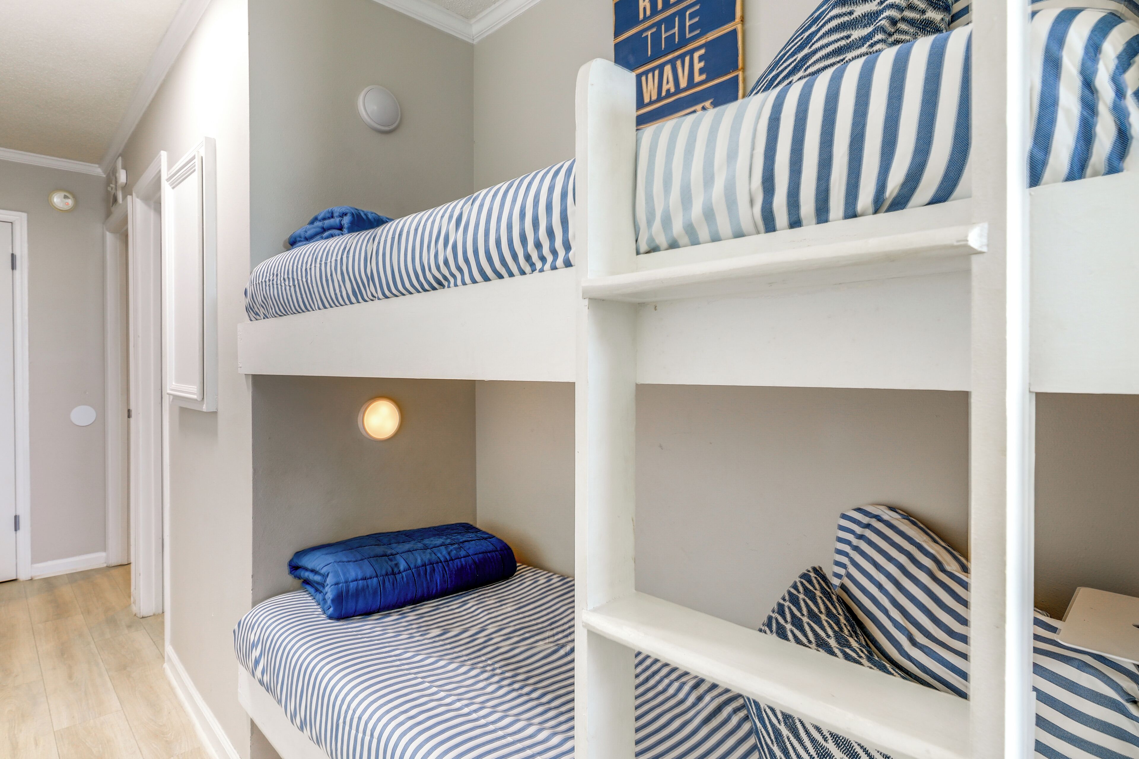 A bunk bed room with striped bedding and a wall sign that reads "Ride the Wave".