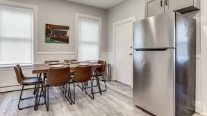 A modern kitchen with a stainless steel refrigerator, wooden dining table, and brown upholstered chairs.