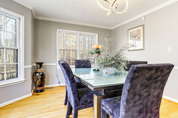 Une salle à manger avec une table en verre, des chaises à motifs foncés, un vase rempli de fleurs et un tableau accroché au mur.