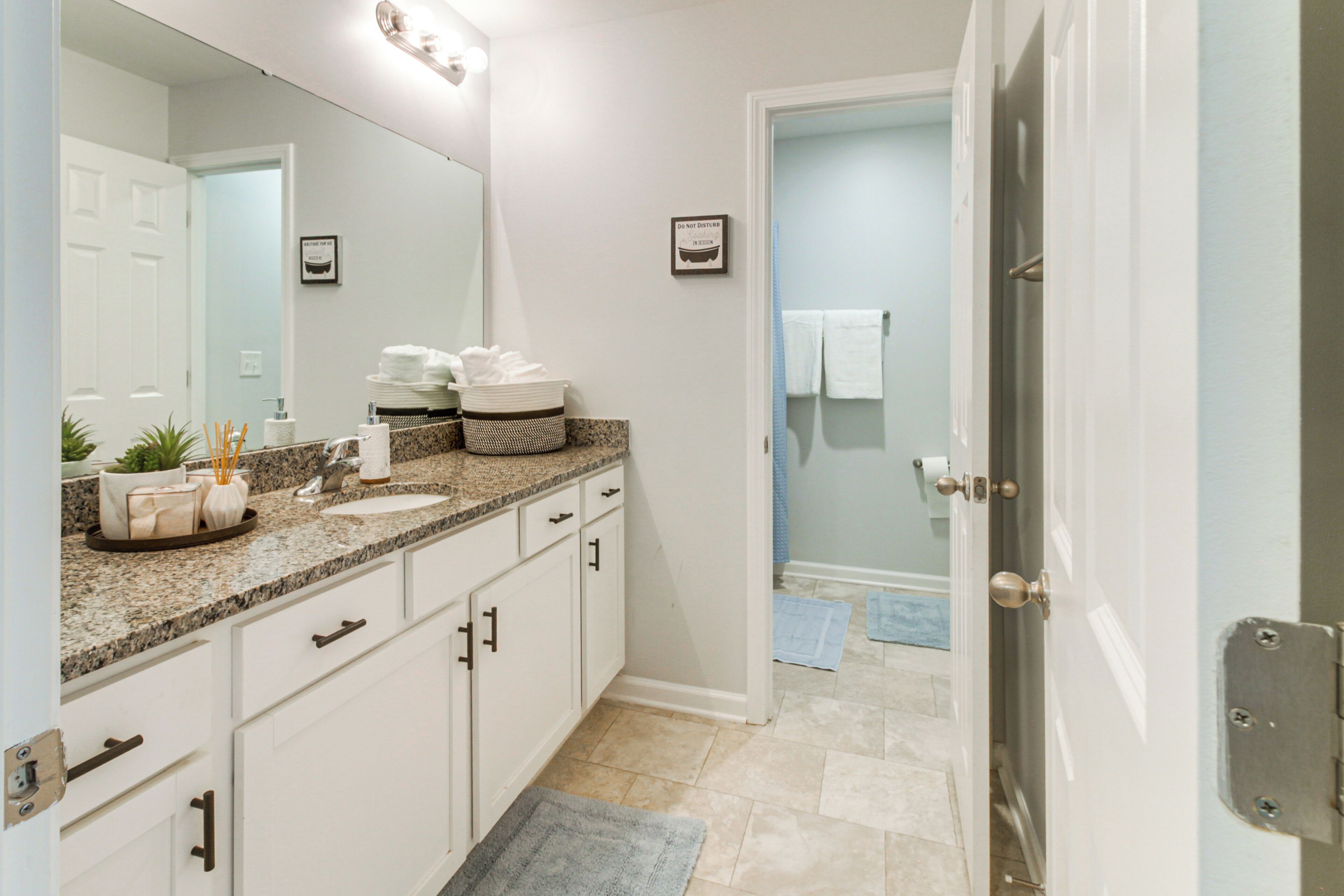 A bathroom with a granite countertop, white cabinets, a large mirror, and a door leading to a shower area.