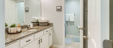 A bathroom with a granite countertop, white cabinets, a large mirror, and a door leading to a shower area.