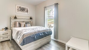 A bedroom with a bed, bedside table, and a window with curtains. - Stay & Play in Charlotte: Family Home w/ Deck (Charlotte)