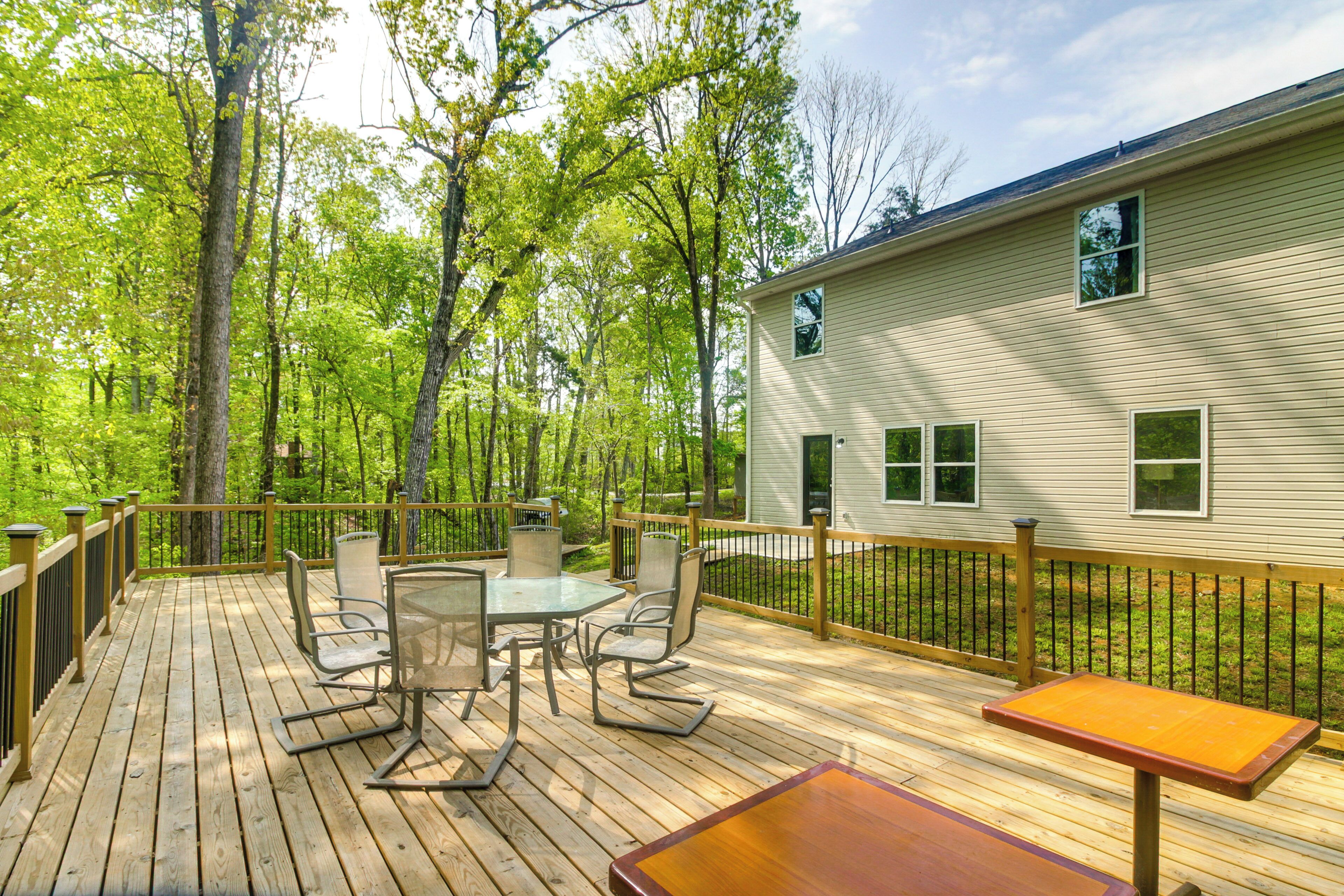 A wooden deck with outdoor furniture, surrounded by trees and a house.