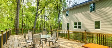 A wooden deck with outdoor furniture, surrounded by trees and a house.