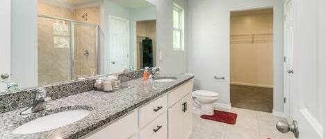 A modern bathroom with a double sink vanity, a large mirror, and a shower area.