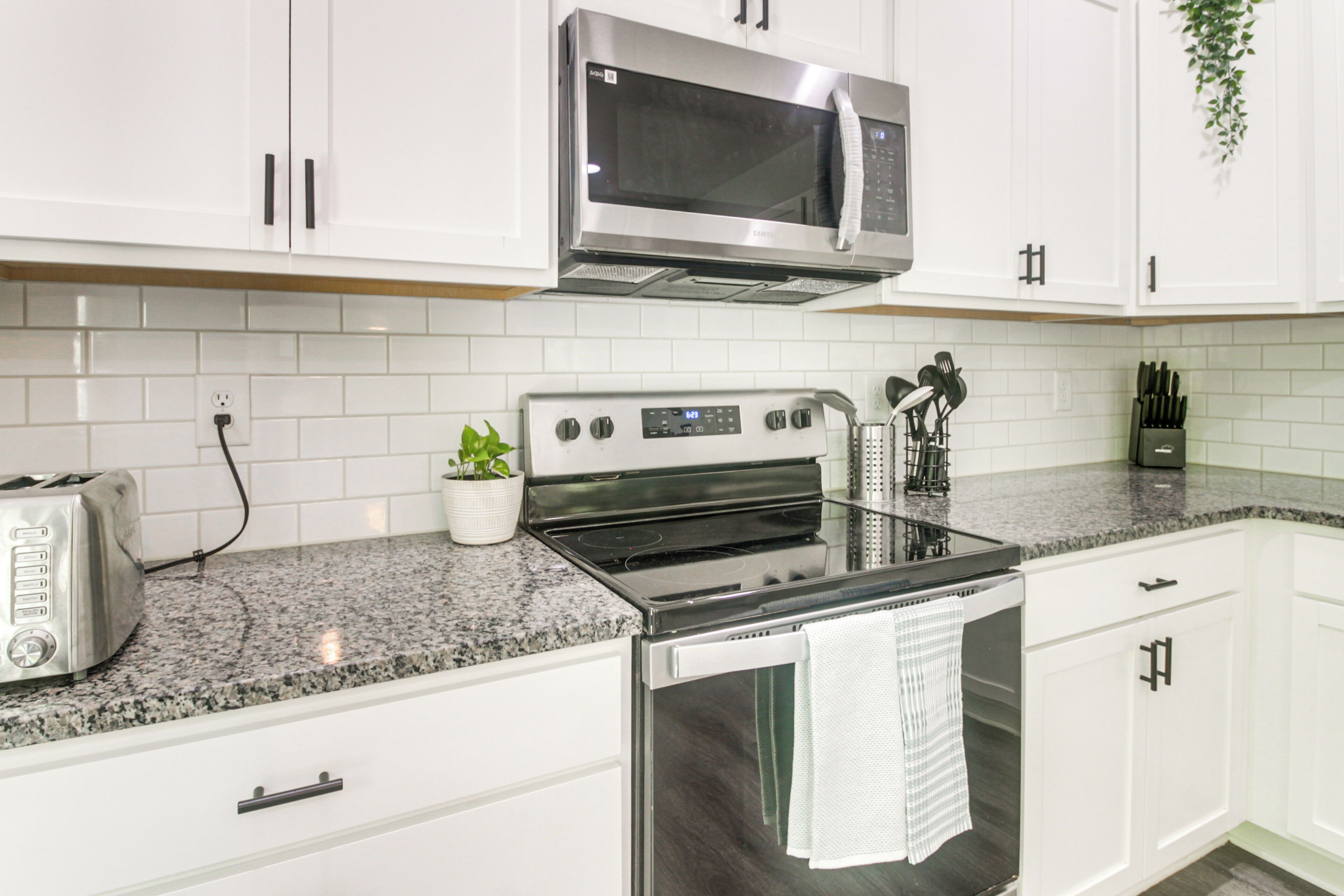 A kitchen with white cabinets, a stainless steel microwave, a stove, and a toaster.
