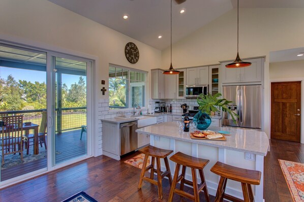 A modern kitchen with a large island, stainless steel appliances, and a sliding glass door leading to a deck.
