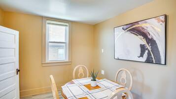 A dining area with a table set for two, a potted plant, and a large abstract painting on the wall.