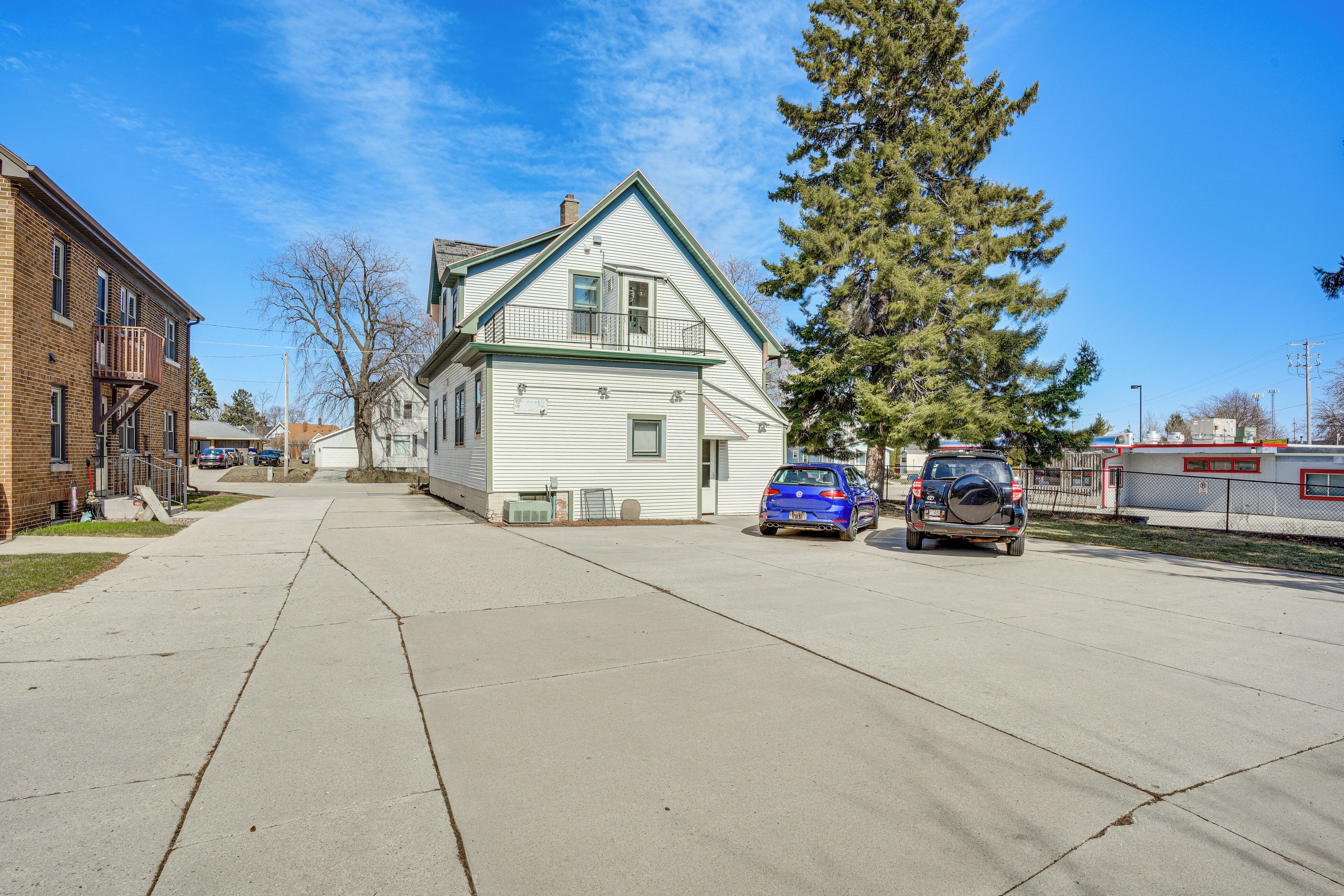 A residential street with a two-story house, parked cars, and a large tree.