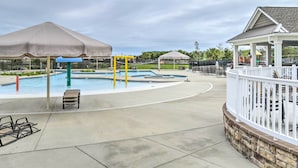 A swimming pool area with umbrellas, lounge chairs, and a gazebo.