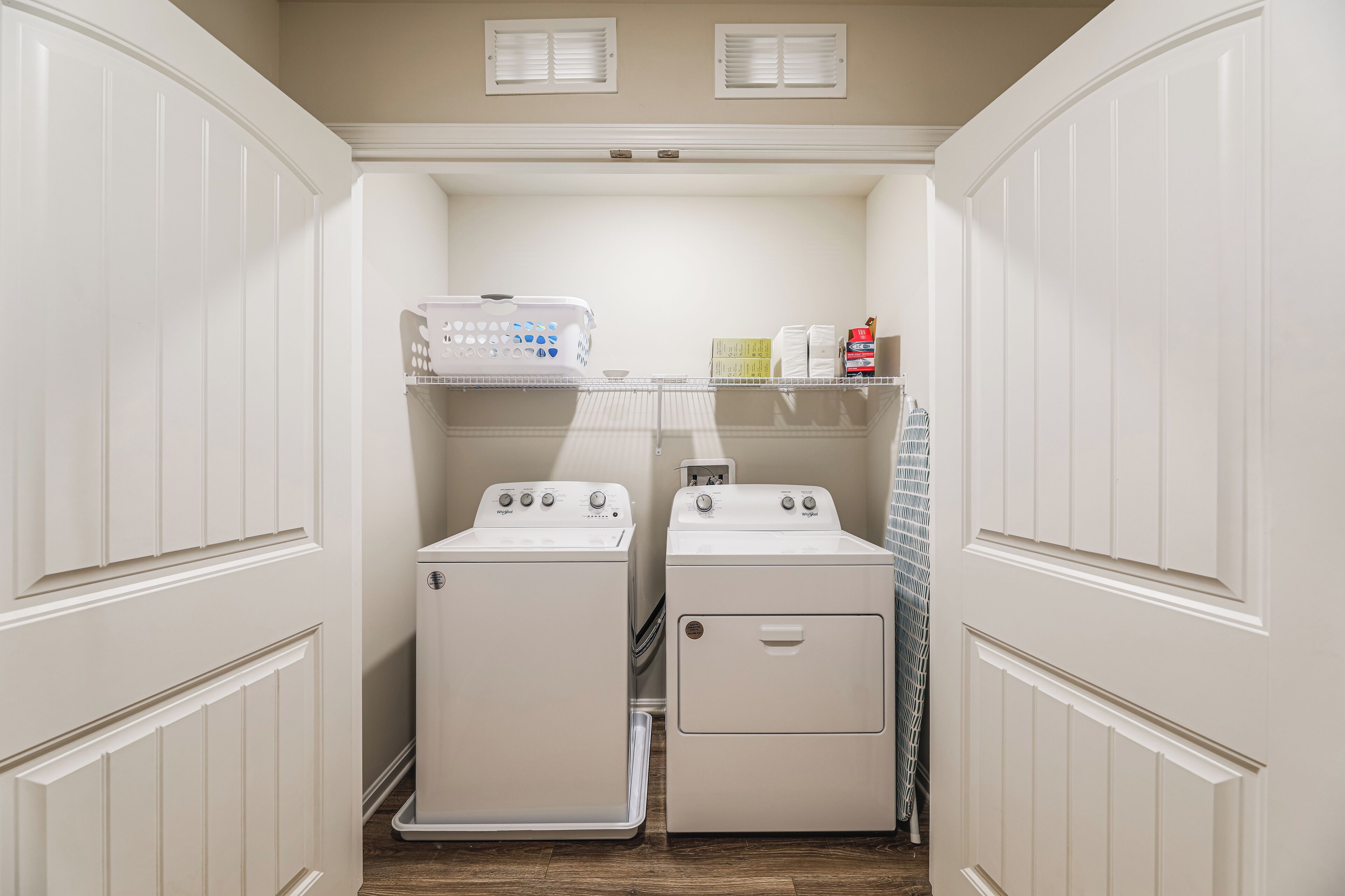 A laundry room with two stacked washers and dryers, a drying rack, and a shelf with laundry supplies.