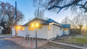 A single-story house with a front porch, a small patio area, and a visible garage. - Farmhouse w/ Horse Corral Near Wind River Arena (Rigby)