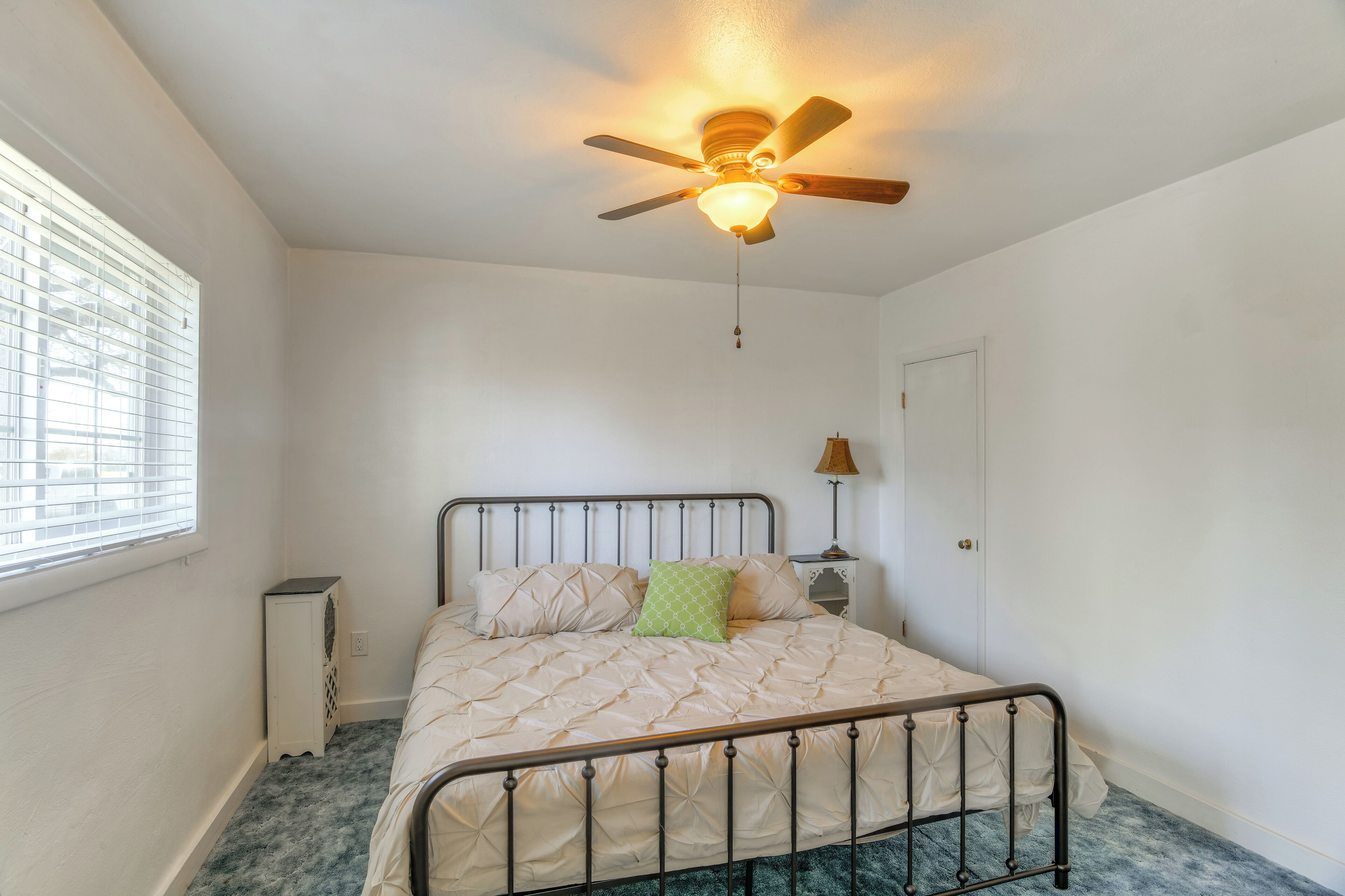 Une chambre à coucher avec un lit, un ventilateur de plafond, une table de chevet et une fenêtre avec des stores.