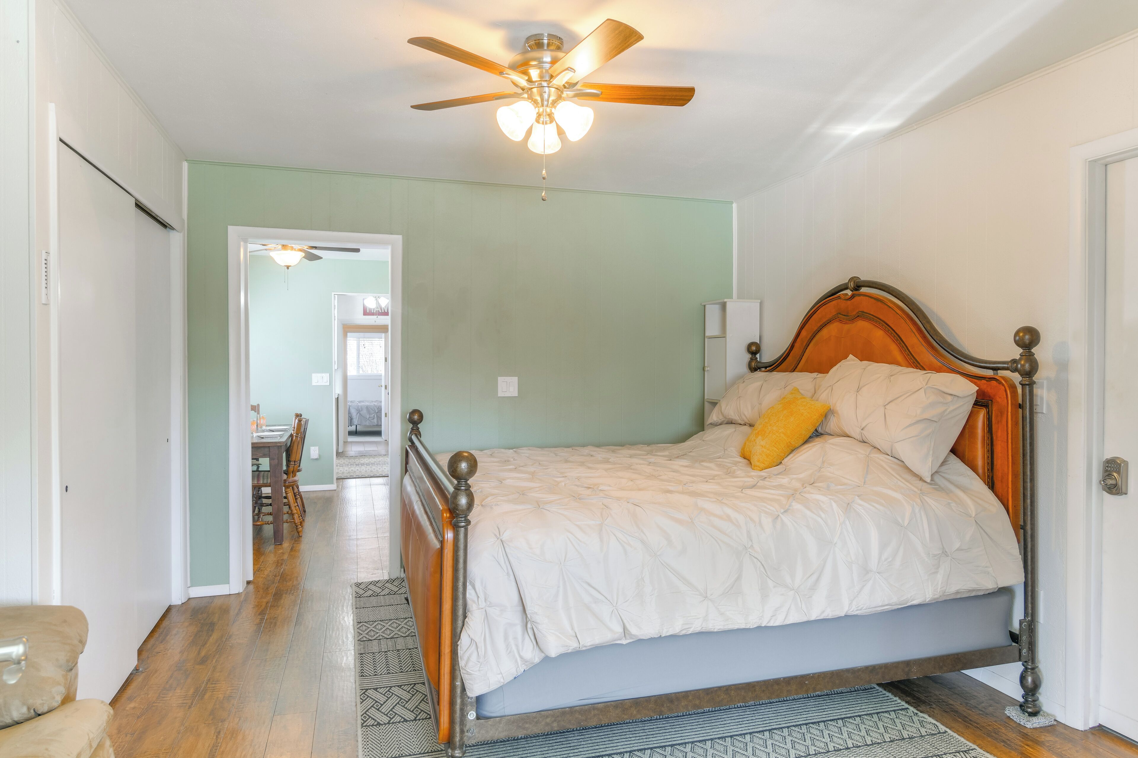 Une chambre à coucher comprenant un lit, un ventilateur de plafond, une porte et un couloir menant à une salle à manger.
