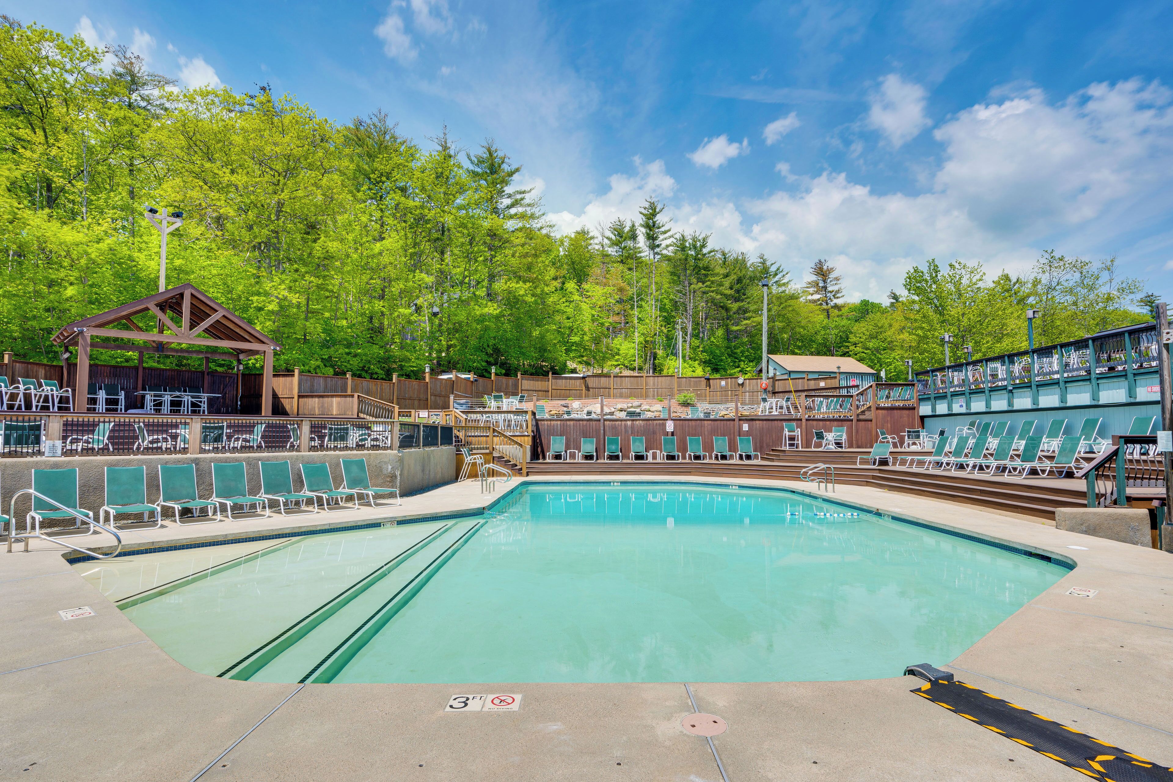 A swimming pool with lounge chairs and a covered seating area, surrounded by trees.